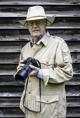 Photographer Weaver Cameron Barksdale in a tan hat and jacket, holding his 35 mm camera.